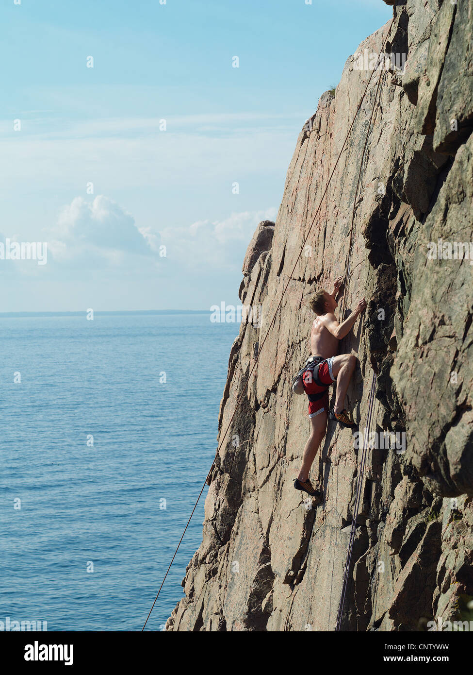 Man scaling coastal rock wall Stock Photo