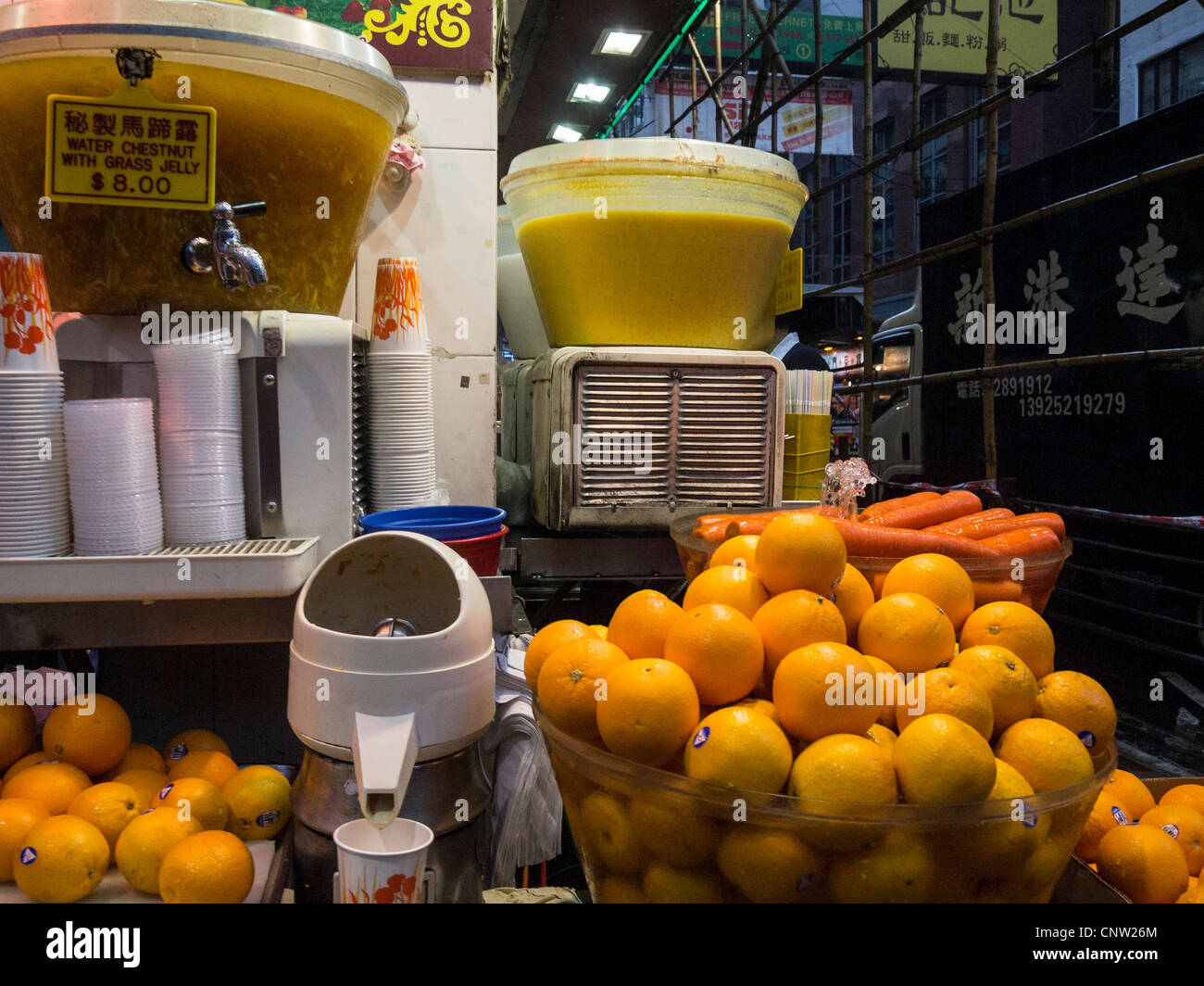 Juice stall on a street corner with oranges and carrots on display and a little fountain playing over the carrots Stock Photo