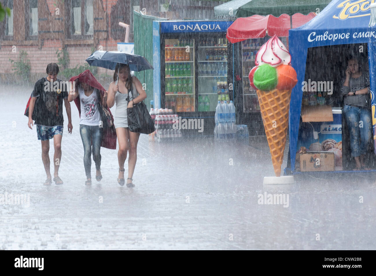 Three young people get caught in a downpour at Hidropark, Kiev, Ukraine, Europe. Stock Photo