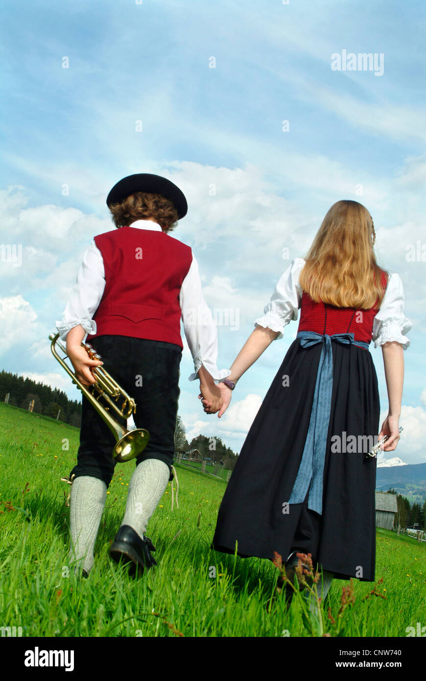 two children in traditional costumes and with musical instruments walking through a meadow hand in hand Stock Photo