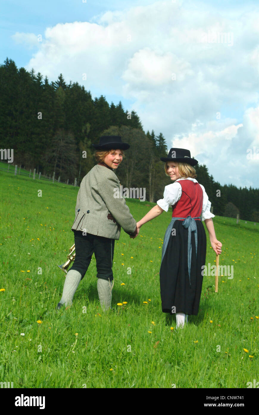 two children in traditional costumes walking through a meadow hand in hand Stock Photo