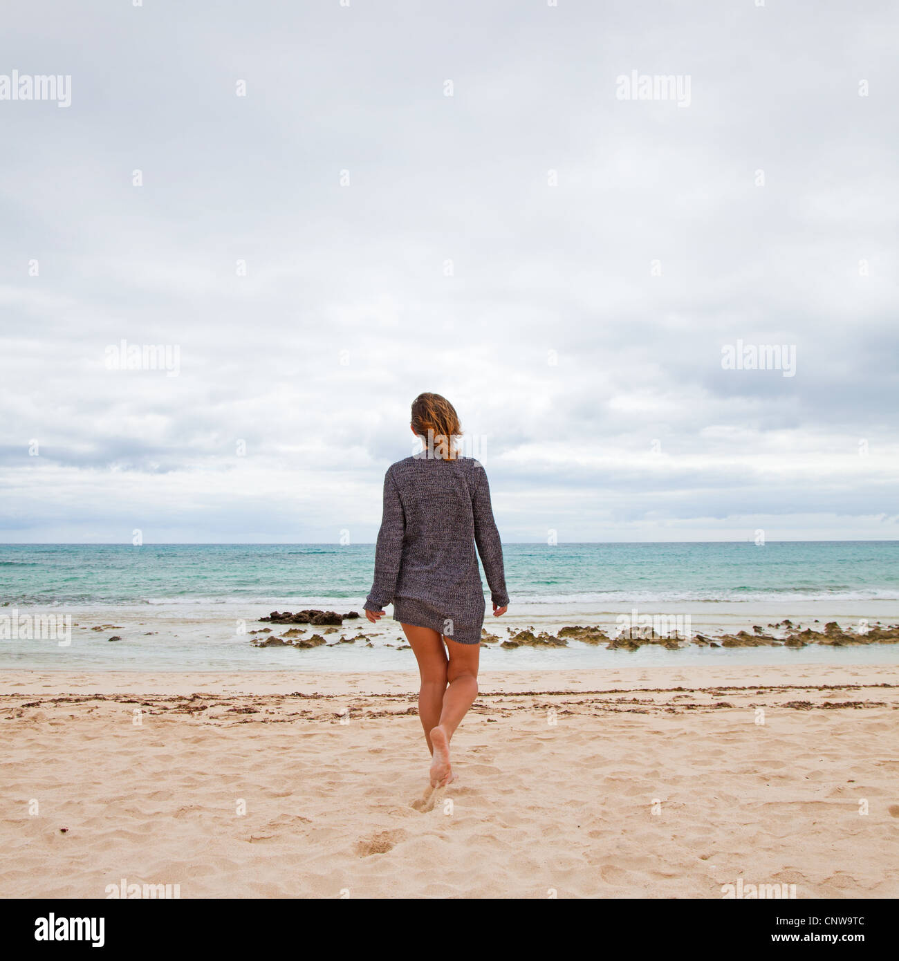 maybe no swimming today - tanned, middle-age woman walks towards the ocean, overcast day Stock Photo