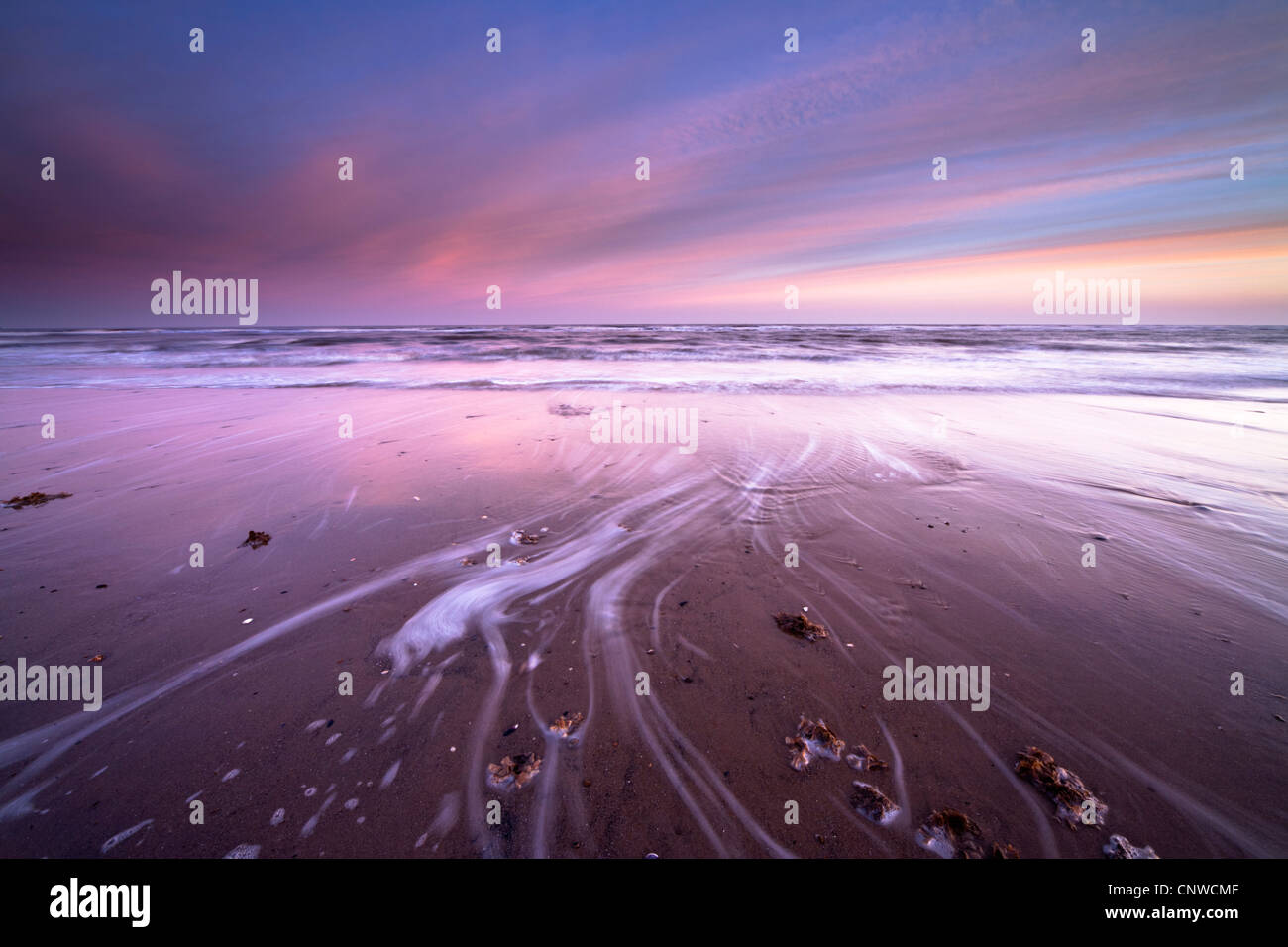 Early morning sunrise casts a pink hue over the incoming tide at Thornham Beach on the Norfolk Coast, UK Stock Photo