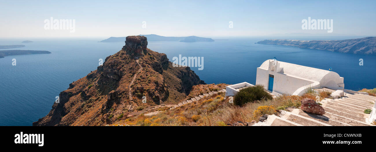 A panoramic image from Santorini of a typical greek church overlooking the rock of skaros with the town of Oia and the volcano i Stock Photo
