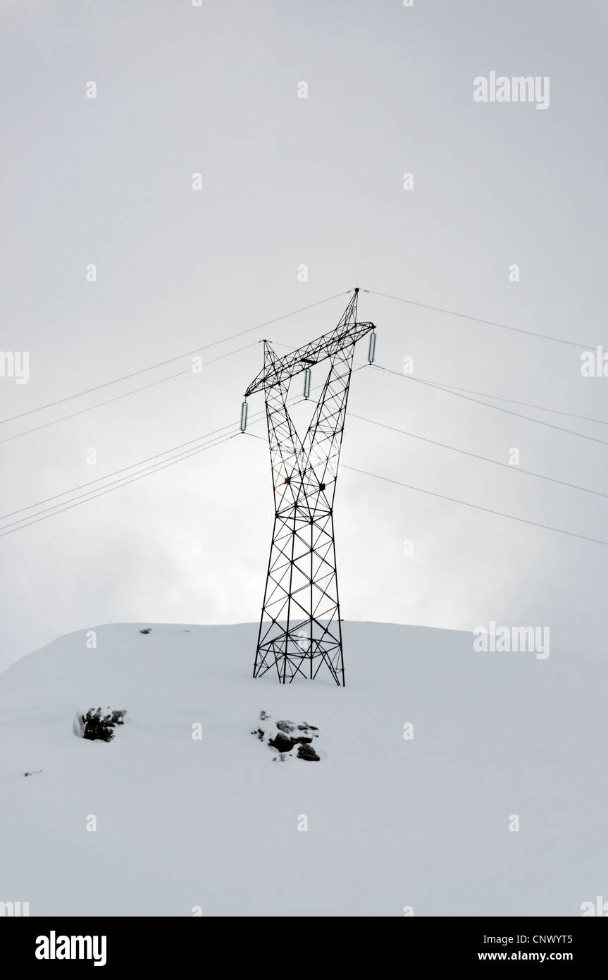 A pylon and power lines in silhouette on a snowy hill Stock Photo