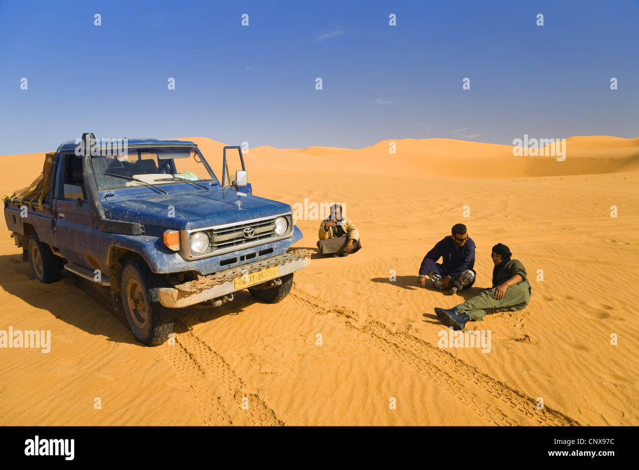 three men resting beside their all-terrain vehicle in the sand desert, Libya Stock Photo