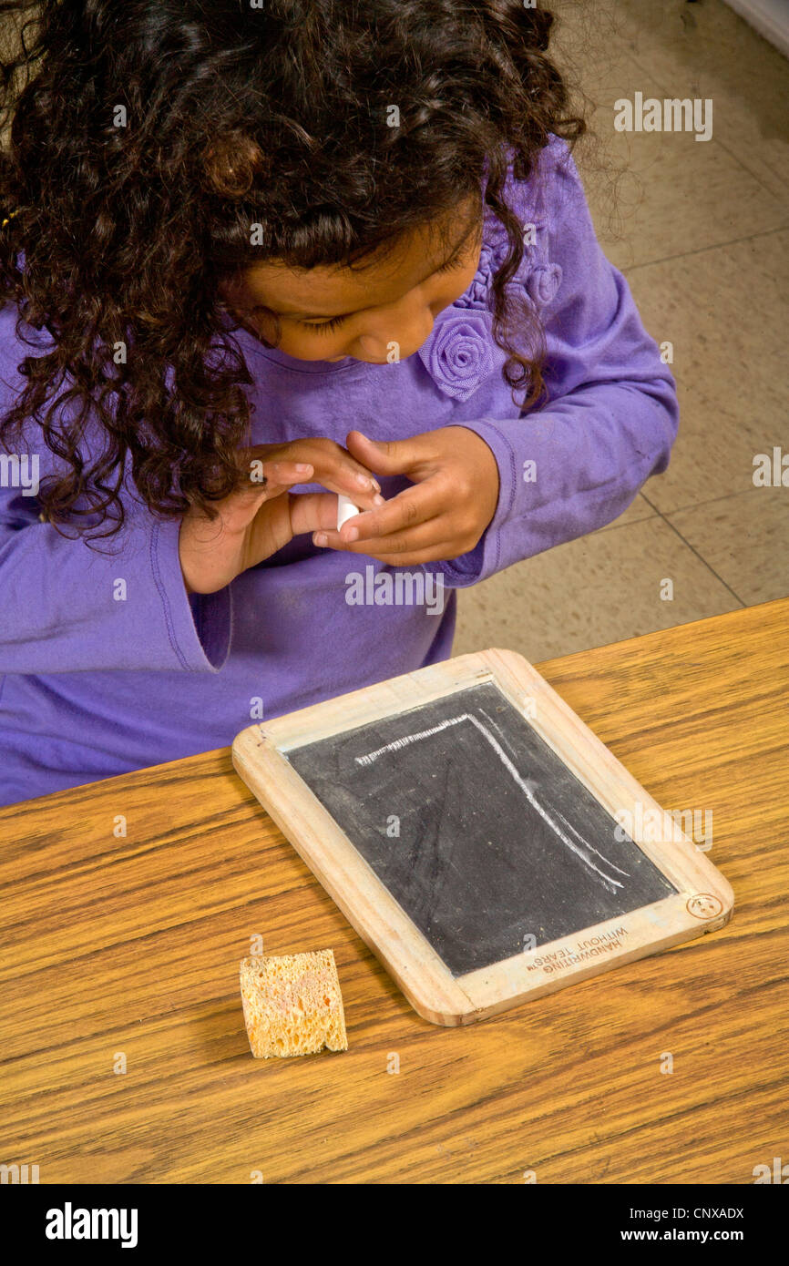 Visually-impaired girl tries to see a large chalked letter 'L' in a special needs writing class for the blind. Stock Photo