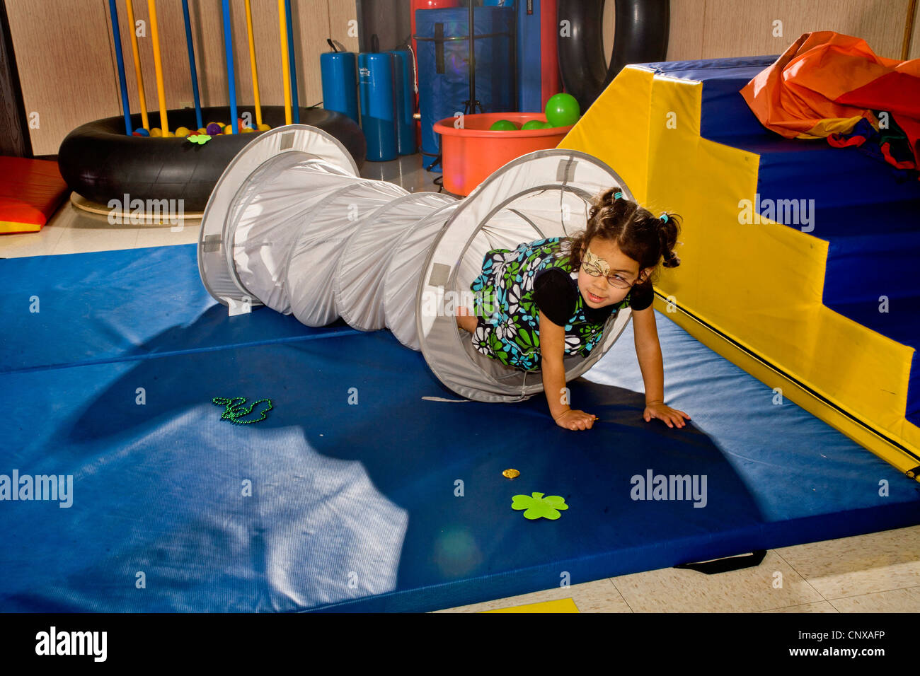 A visually-impaired girl crawls through a tunnel to improve body sensitivity in a sensory motor group. Stock Photo