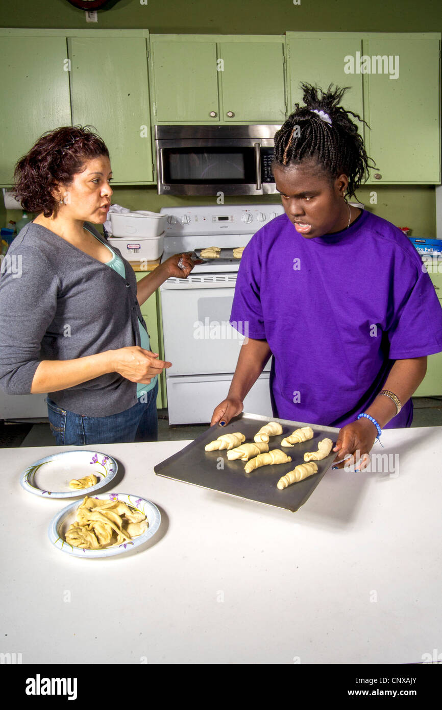 Assisted by a teacher, a blind African-American preteen girl makes rolls by touch from prepared dough in a cooking class. Stock Photo
