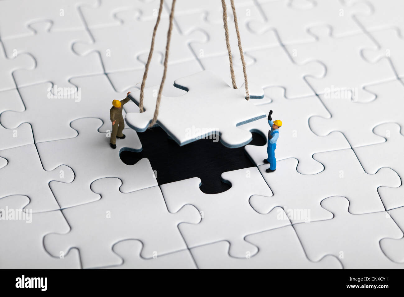 Miniature workmen guiding a hanging puzzle piece into place Stock Photo