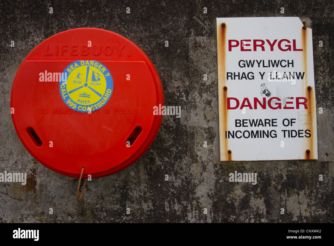 Red lifebuoy and  signs in English and Welsh warning of danger of incoming tides. Stock Photo