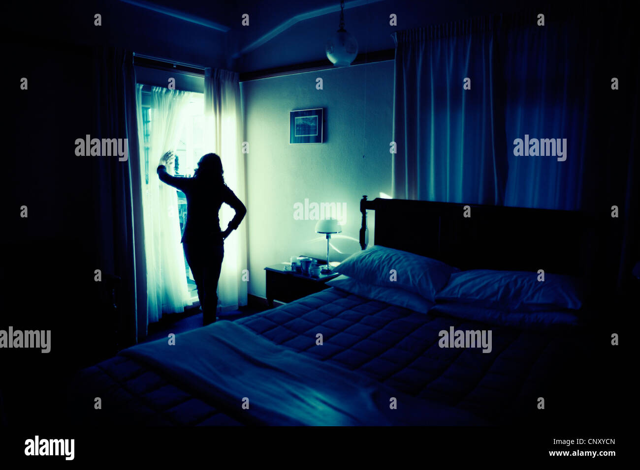 Woman looks out of french doors in bedroom. Stock Photo