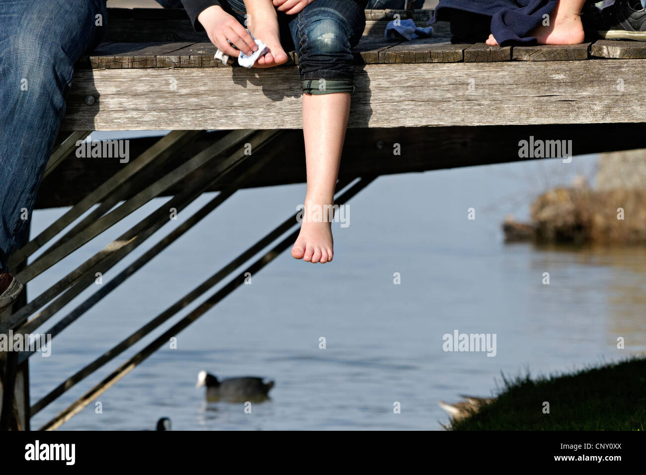 Girl drying her foot with a sock with one leg hanging down from a pier, Prien Stock Chiemgau Upper Bavaria Germany Stock Photo