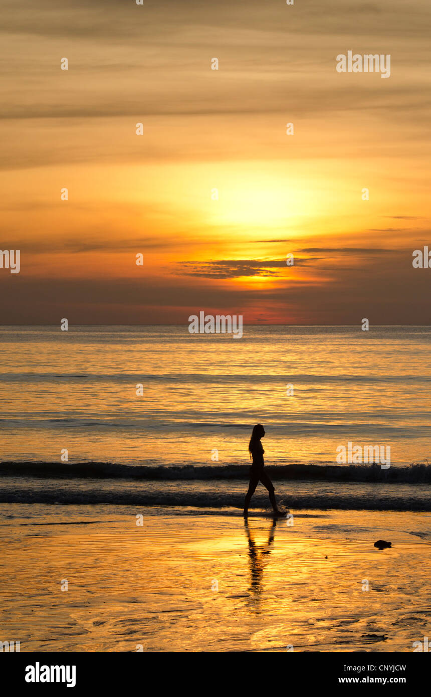 Woman in silhouette walking along a beach at sunset hi-res stock ...