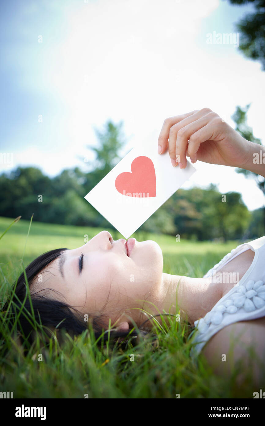 A woman lying on green field with heart card Stock Photo