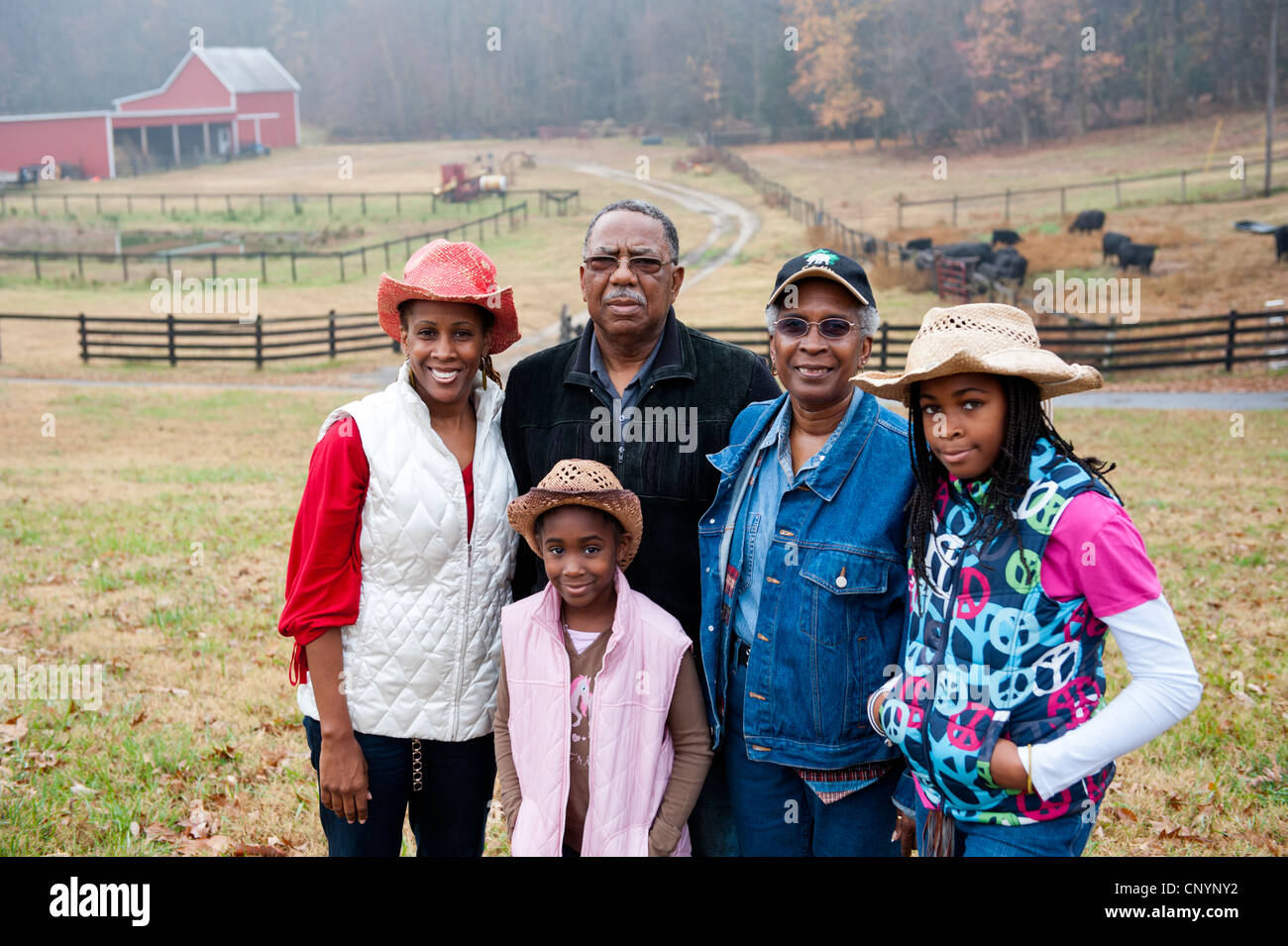 Farm family stands happily against farm landscape. Stock Photo
