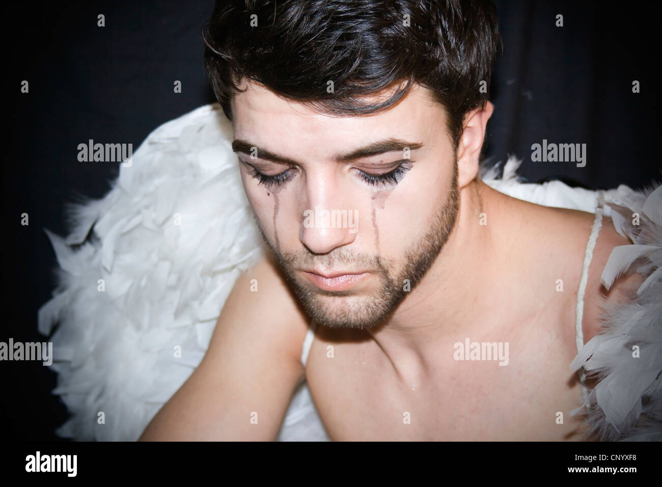 Sad young man with black streaked eye makeup, wearing angel's wings Stock Photo