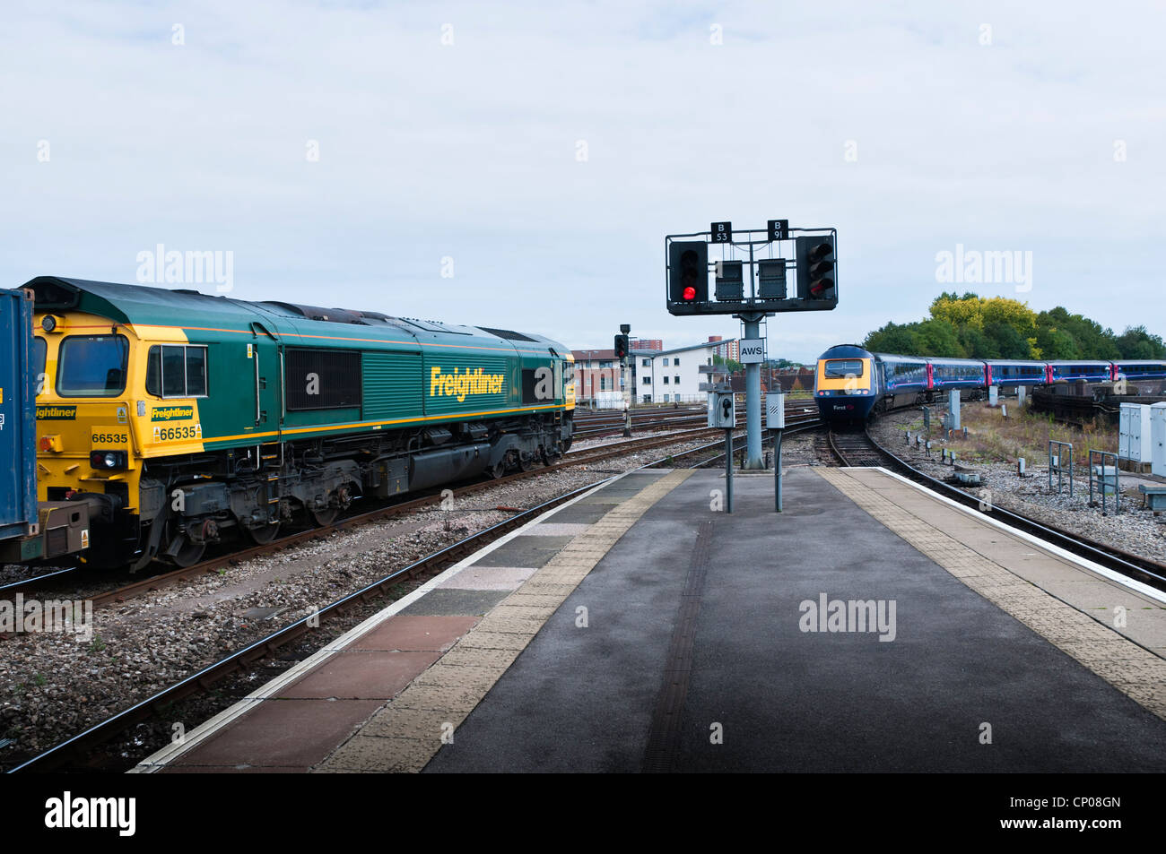 A  Freightliner Class 66 locomotive heading a train of container freight wagons, while a passenger train leaves on another line. Stock Photo