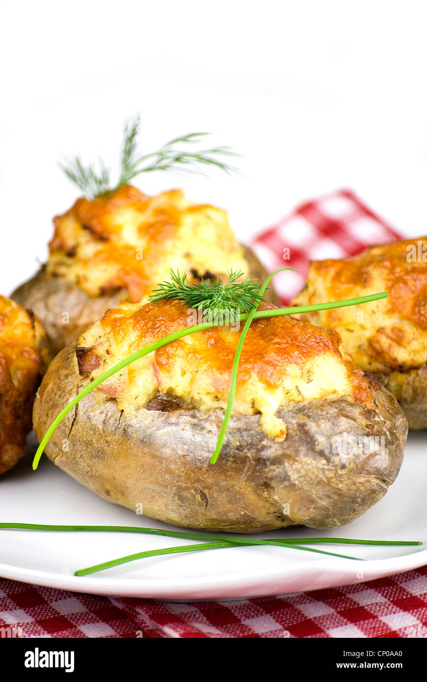 stuffed potatoes covered with cheddar cheese decorated with chives and dill leaves in a white plate Stock Photo
