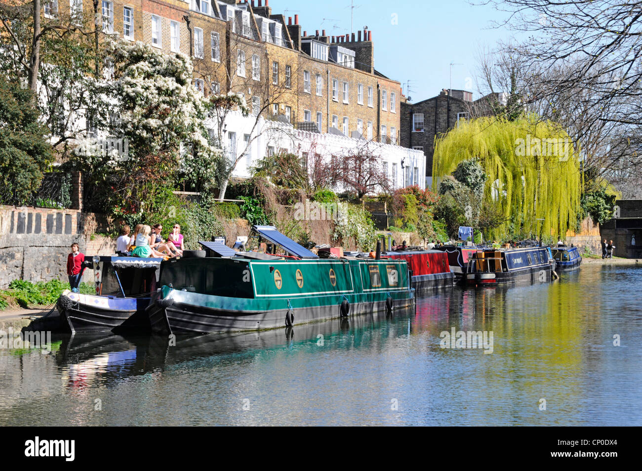 Sunny Regents Canal narrowboat moorings & real estate property people walking towpath spring colour on Weeping Willow tree Islington London England UK Stock Photo
