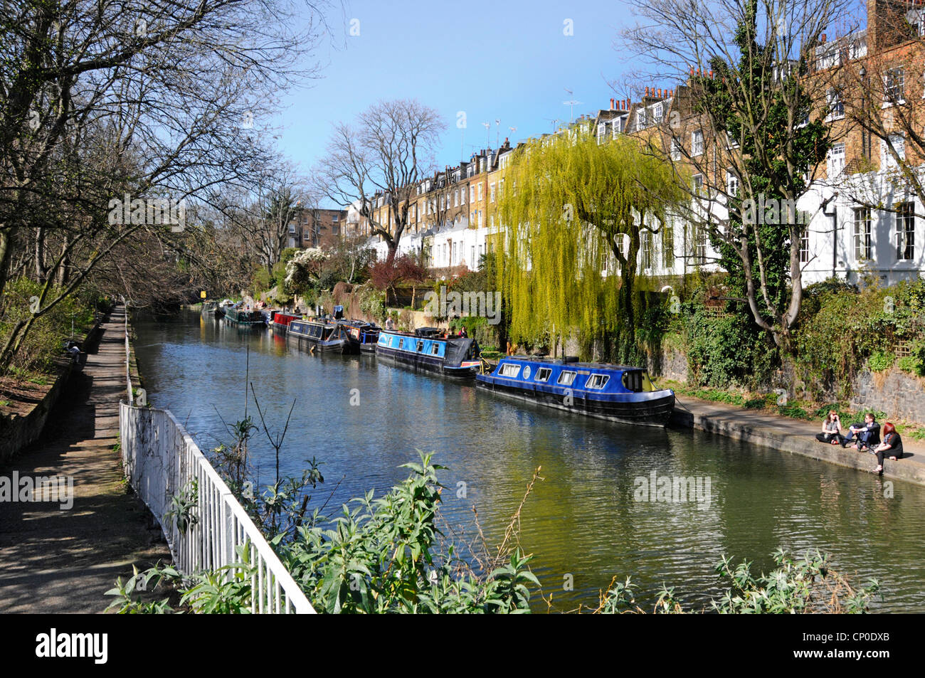 Sunny Regents Canal narrowboat moorings & real estate property people walking towpath spring colour on Weeping Willow tree Islington London England UK Stock Photo