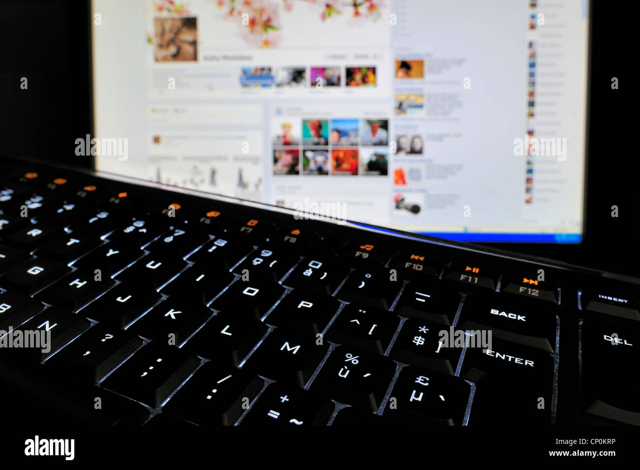 Black computer keyboard with illuminated backlit white characters on keys and pc screen in the dark Stock Photo