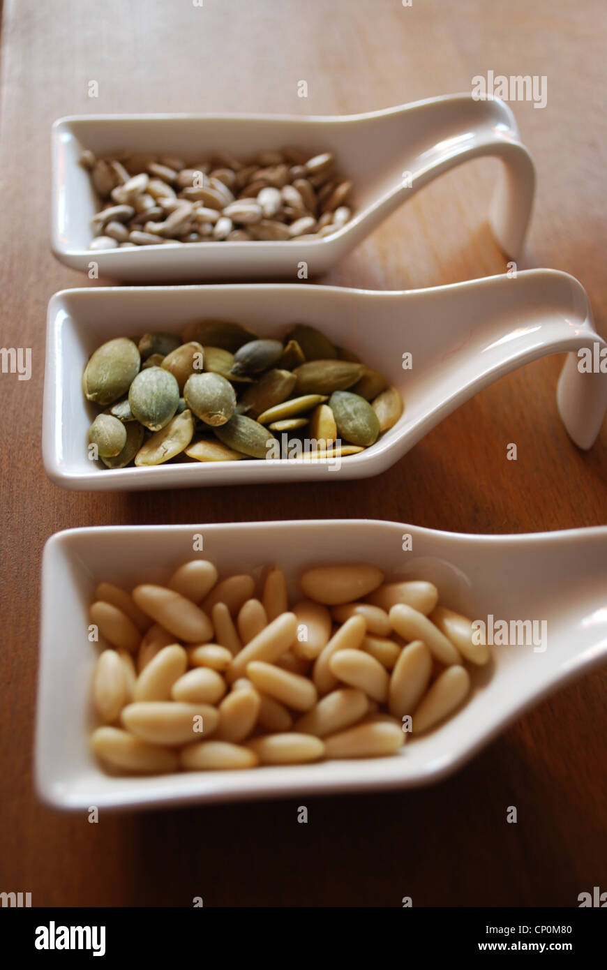 Edibles pine nuts, pumpkin and sunflower seeds in three white ceramic containers on natural wooden table background Stock Photo