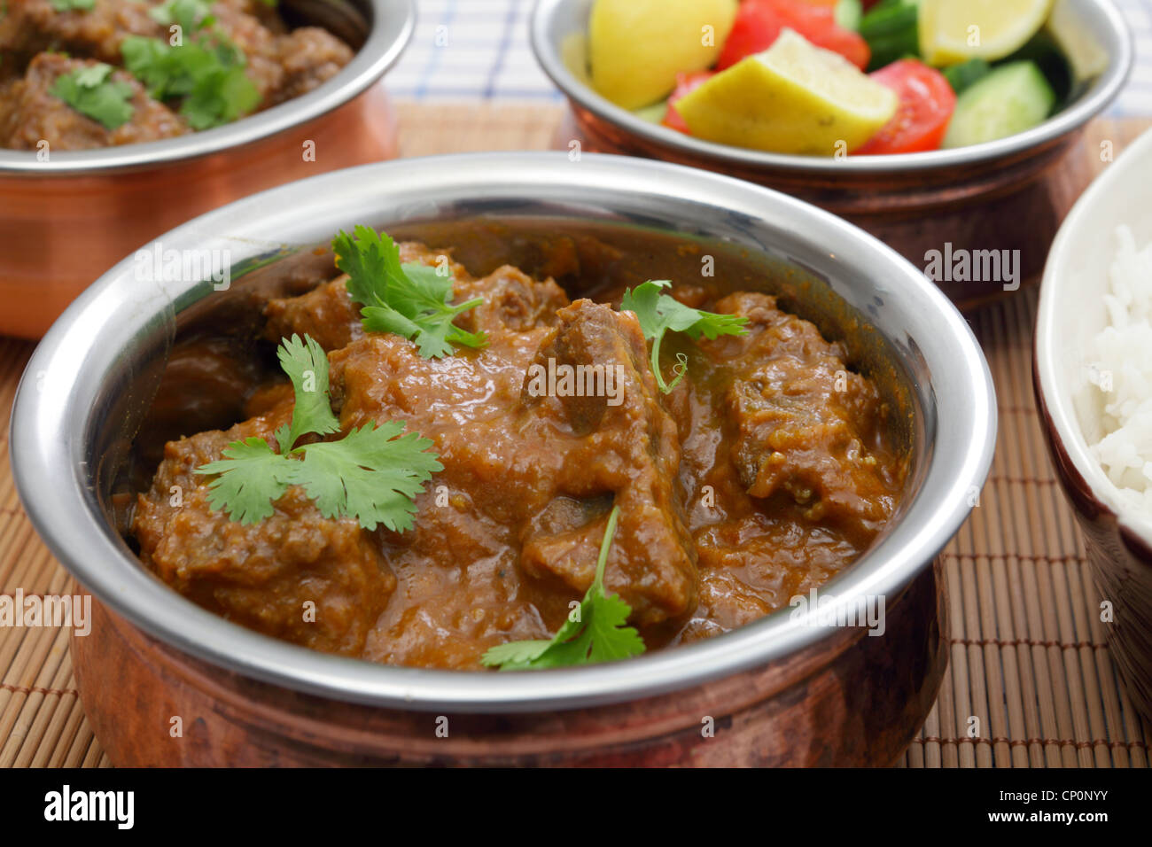 A bowl of Madras butter beef curry with rice, salad and another curry ...