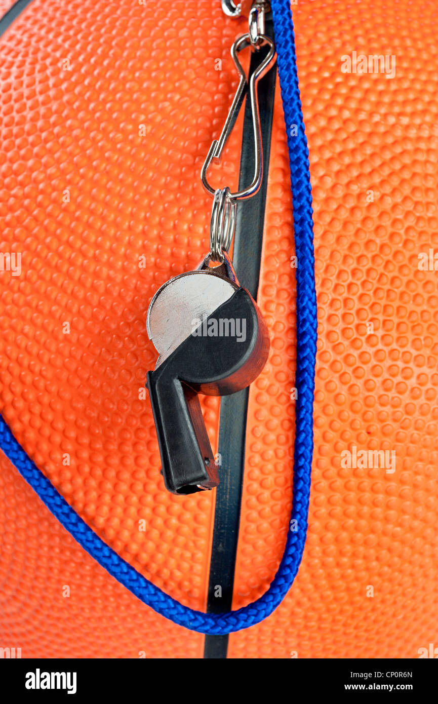 A basketball referee's whistle draped over an orange, rubber basketball. Good for sports inferences where rules are important. Stock Photo