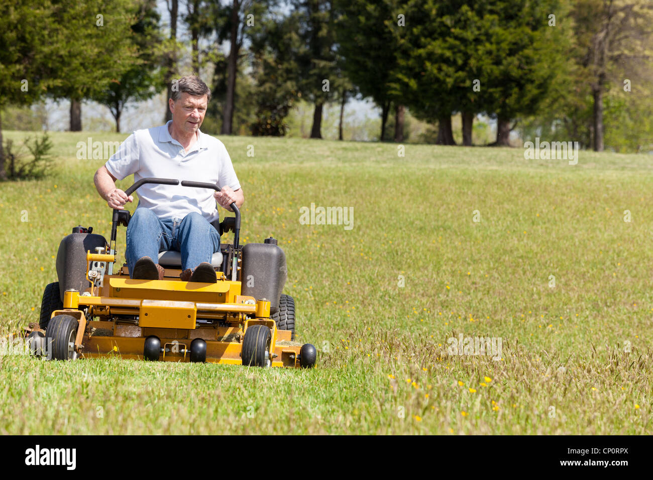 Senior retired male cutting the grass on expansive lawn using yellow zero-turn mower Stock Photo