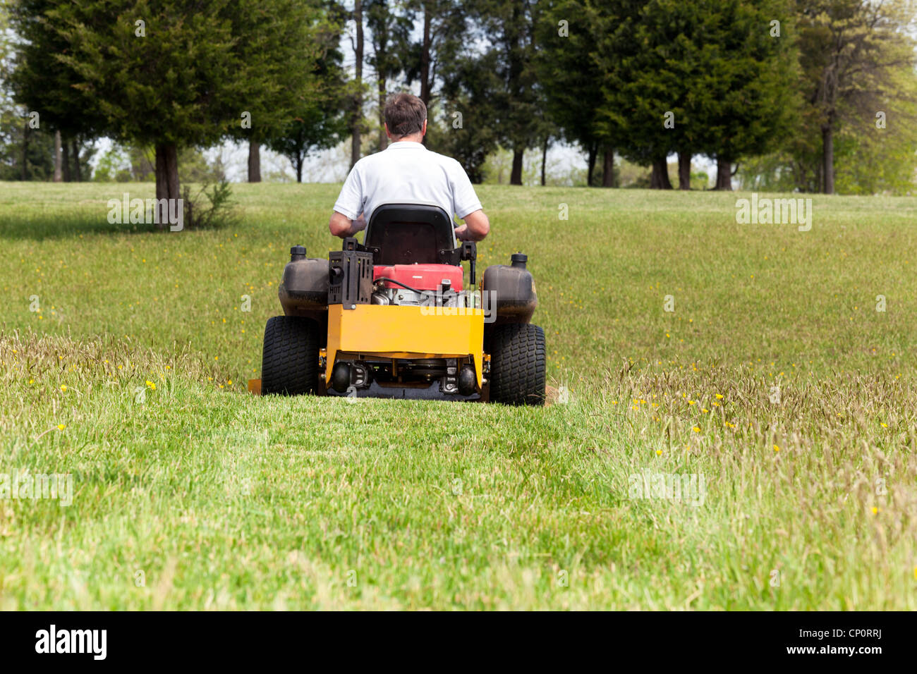 Senior retired male cutting the grass or mowing lawn on an expansive lawn using yellow zero-turn mower Stock Photo