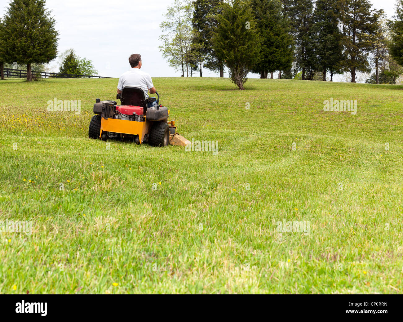 Senior retired male cutting the grass on expansive lawn using yellow zero-turn mower Stock Photo