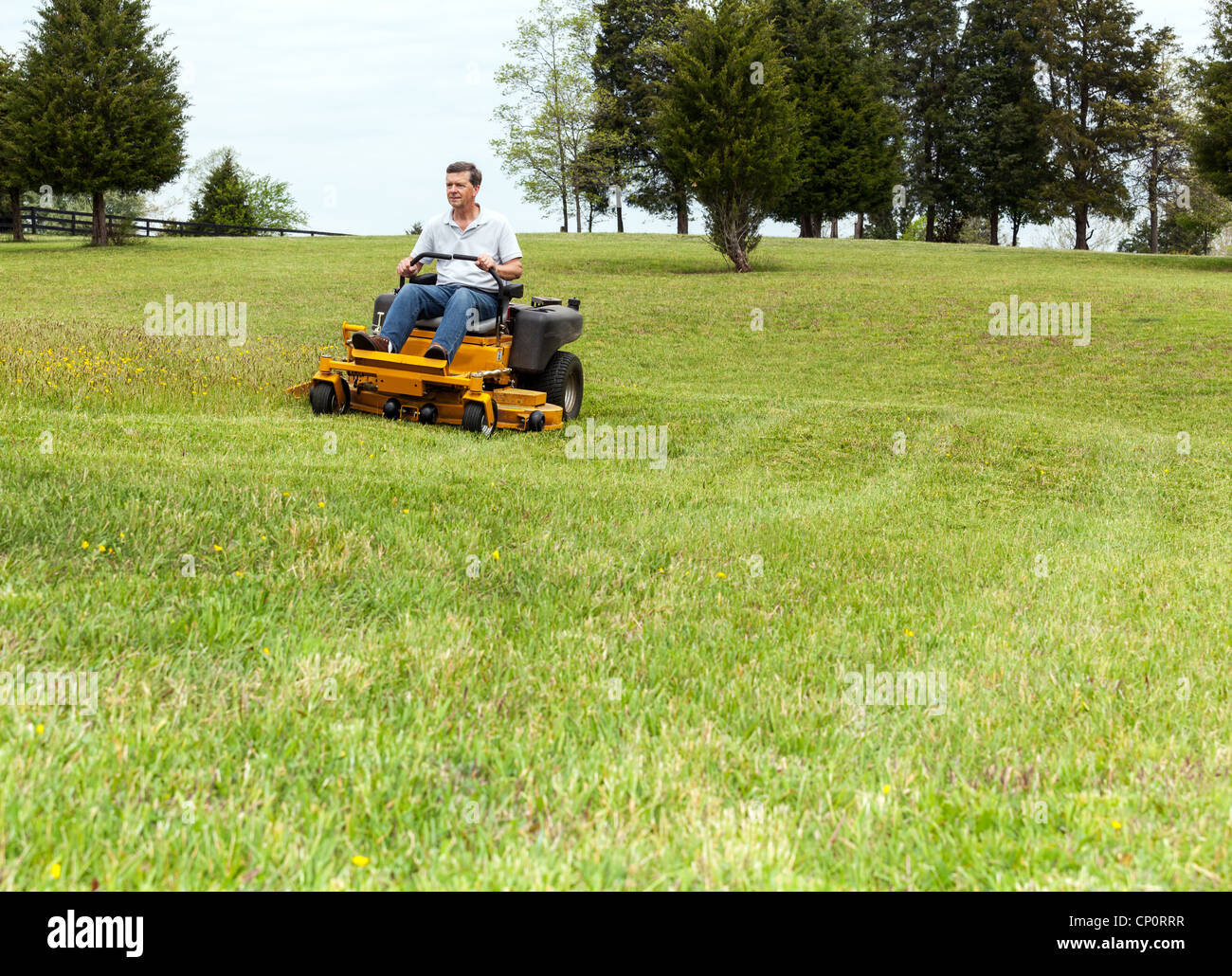 Senior retired male cutting the grass on expansive lawn using yellow zero-turn mower Stock Photo