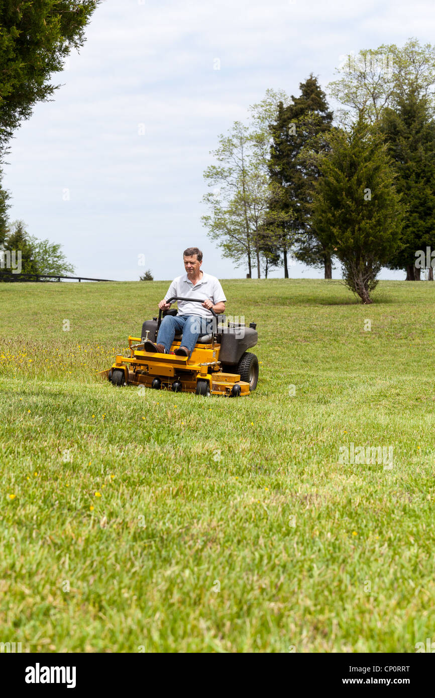 Senior retired male cutting the grass on expansive lawn using yellow zero-turn mower Stock Photo