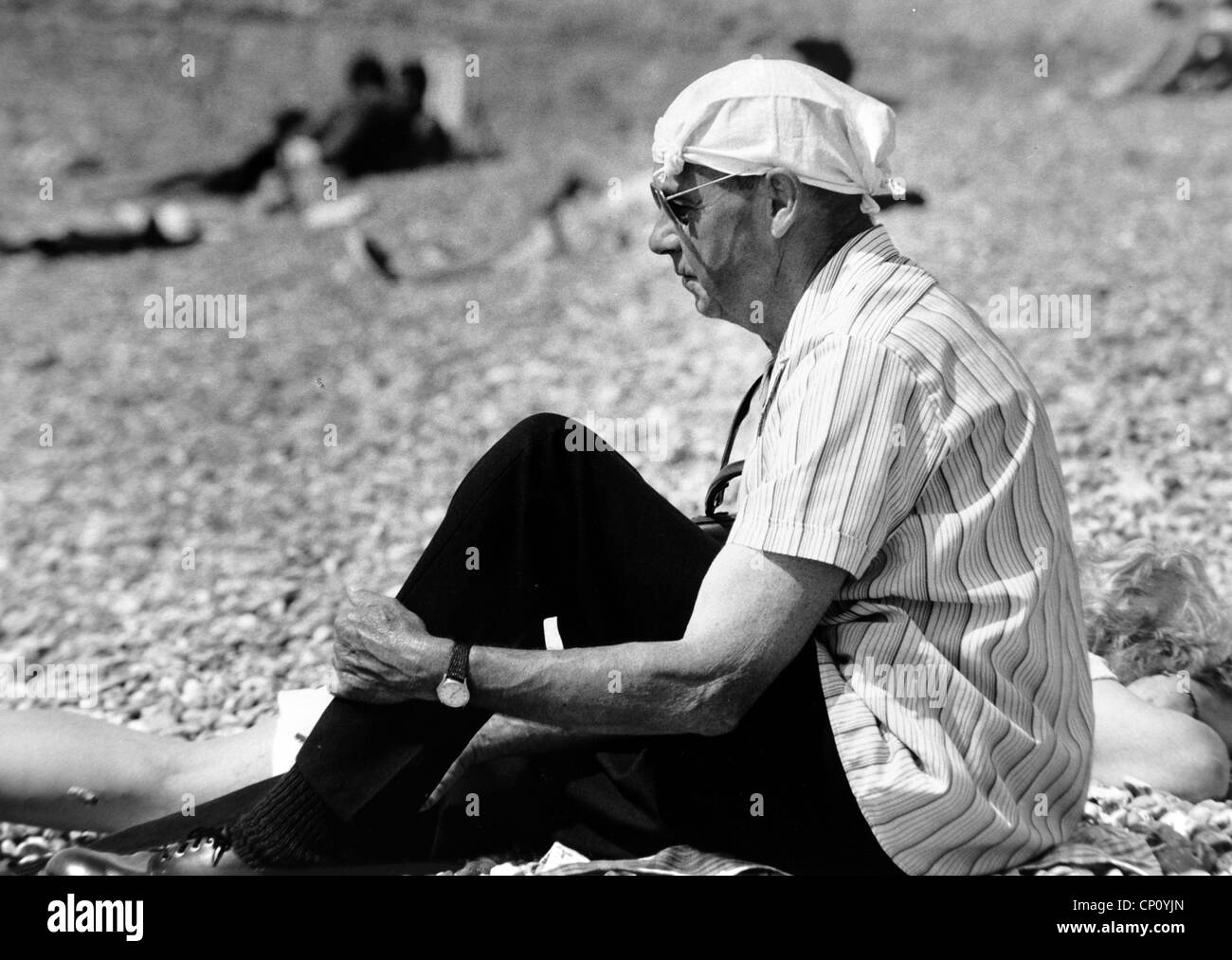 Man sitting in the sun on Brighton beach wearing a handkerchief on his head for protection 1988 Stock Photo