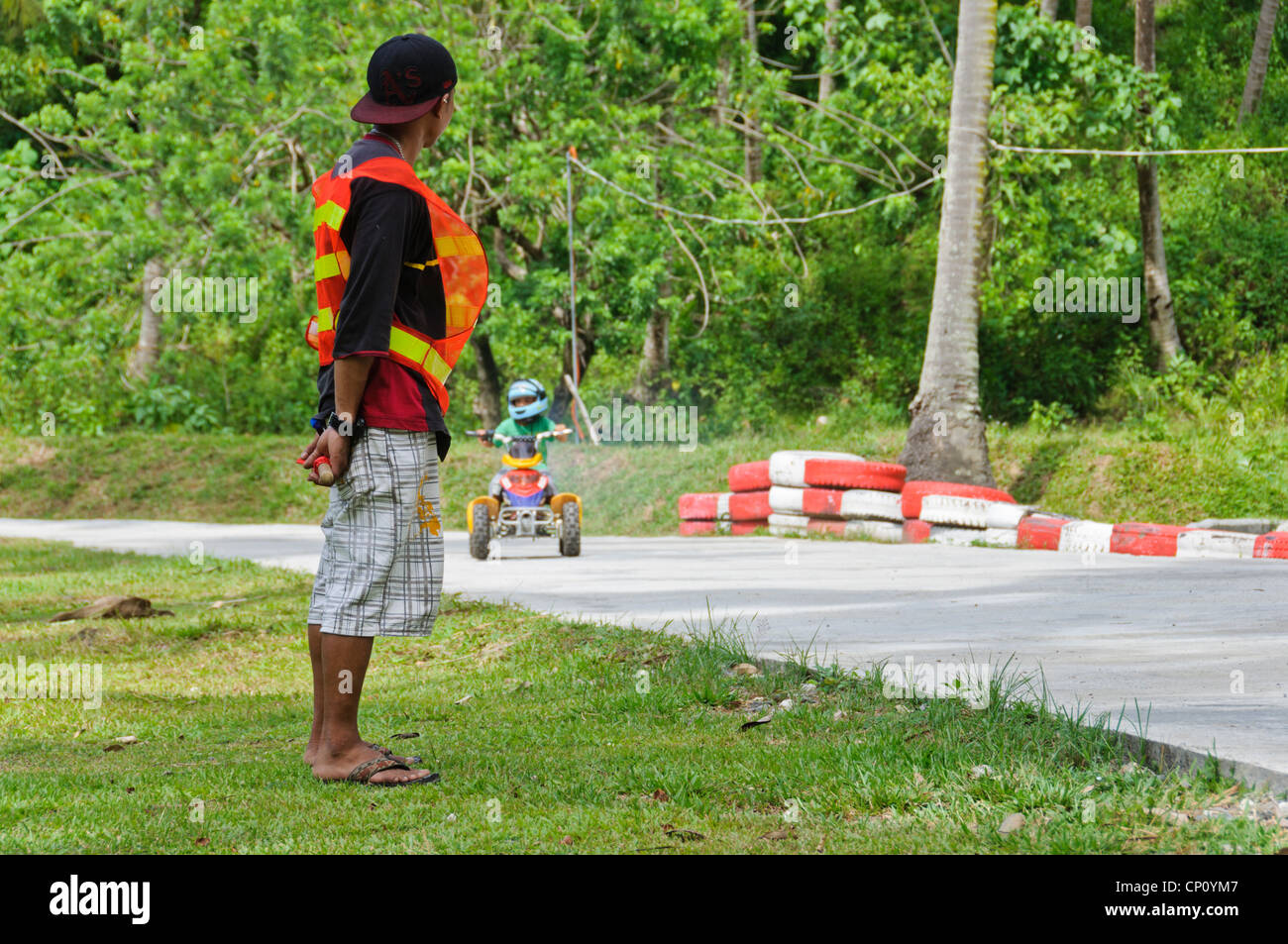 Asian Track Marshal looking at little boy driving ATV Adventure Park Puerto Galera Oriental Mindoro Philippines Southeast Asia Stock Photo