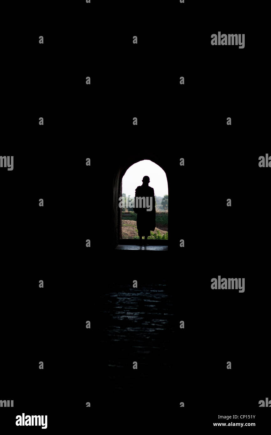 Monk standing, silhouetted in an arched shaped temple doorway, Burma Myanmar Stock Photo