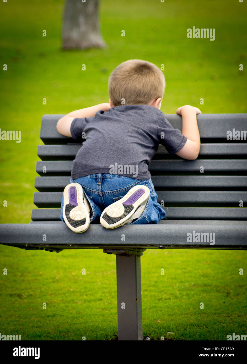 A 4 year old boy with Autism crouches backwards on a bench by the beach. Stock Photo