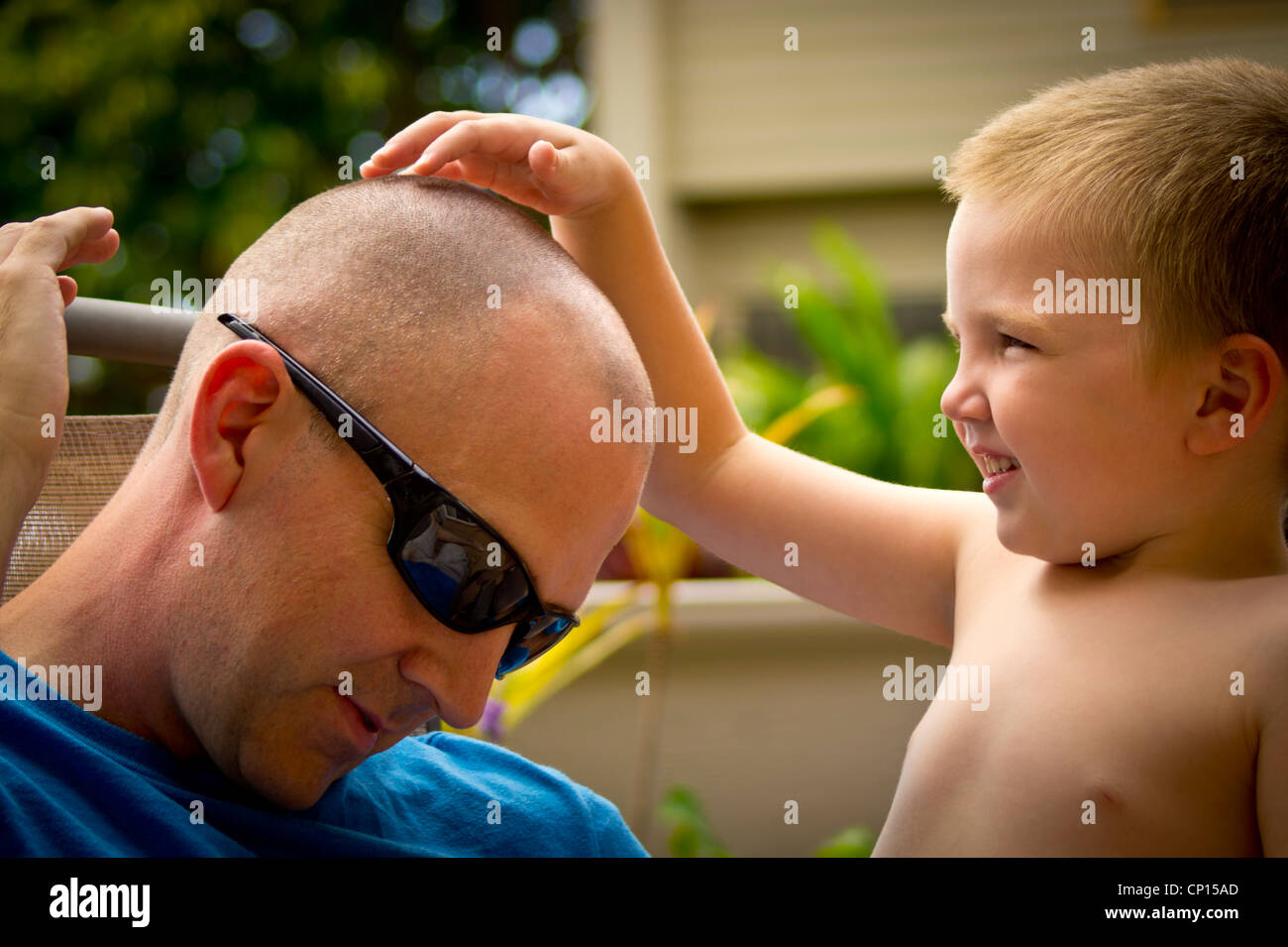 An autistic boy lightly touches the top of his father's recently cut hair. Stock Photo