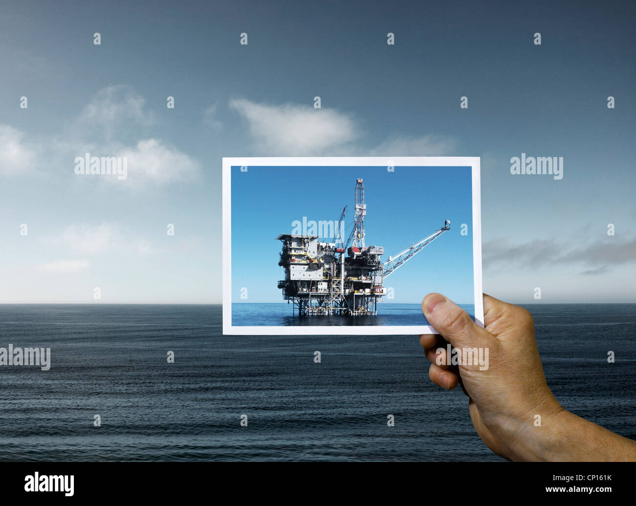 Hand Holding Photograph of Oil Platform over Ocean Stock Photo