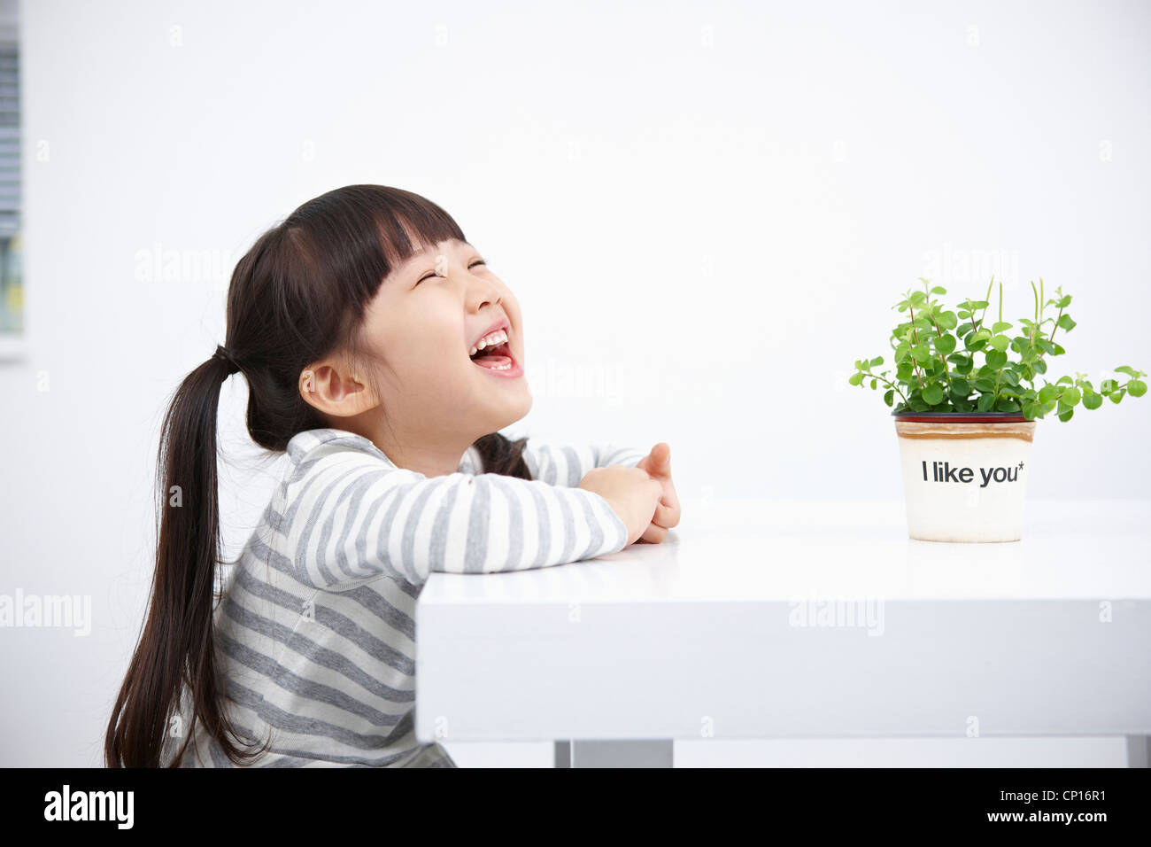 Smiling girl with green plant on the table Stock Photo - Alamy