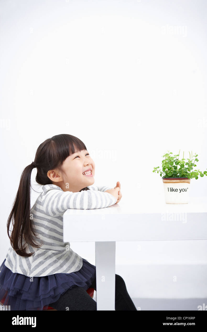 Smiling girl with green plant on the table Stock Photo - Alamy