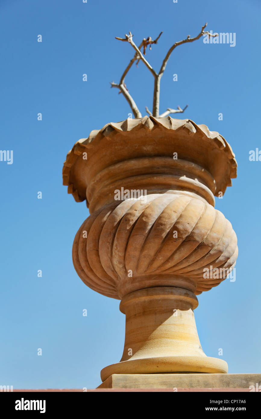 Upward view point of indigenous Rajasthan stone carved and crafted plant pot with stick plant on a clear blue cloudless sky Stock Photo