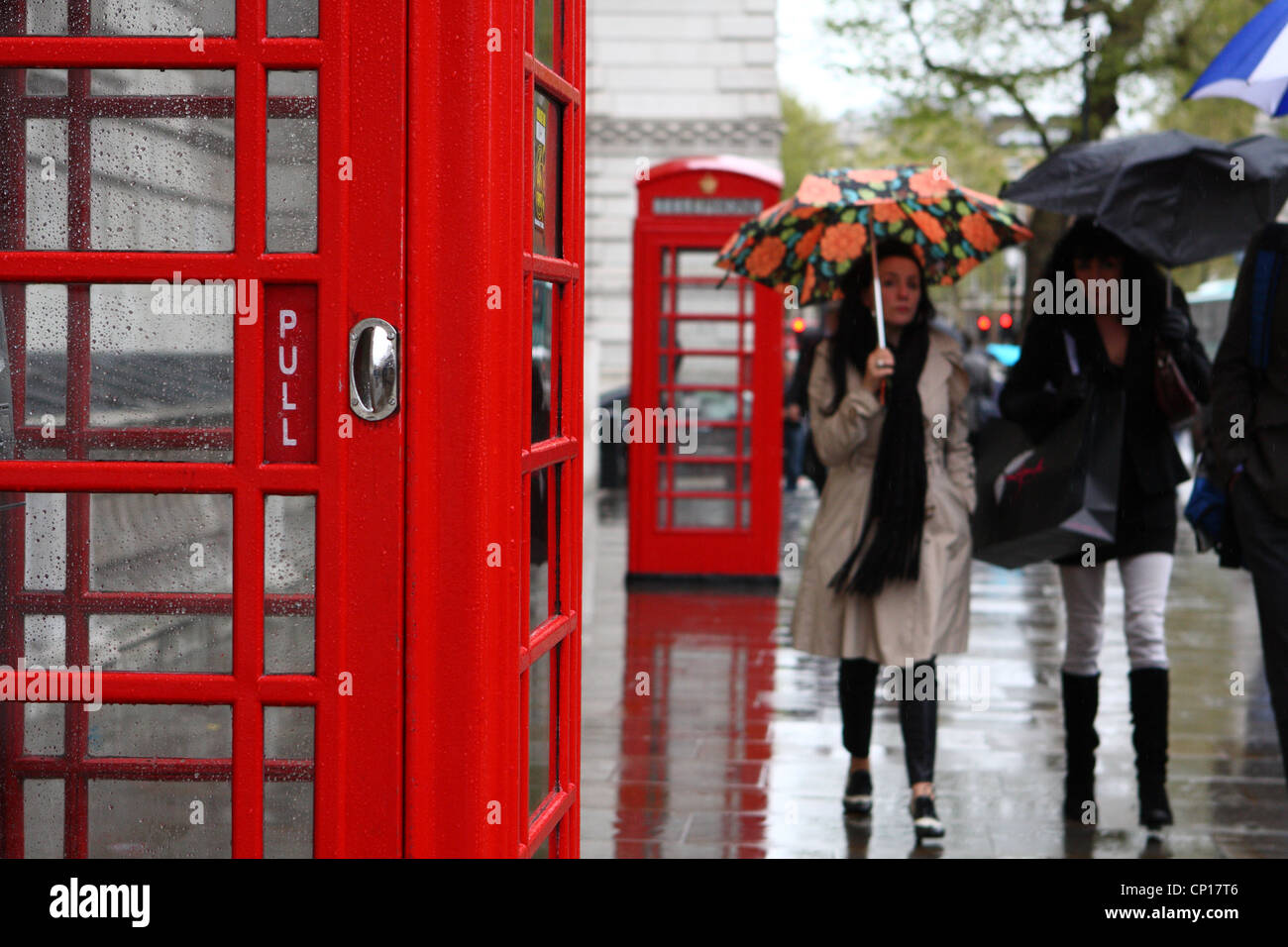 people walking in the rain passed red telephone boxes Stock Photo