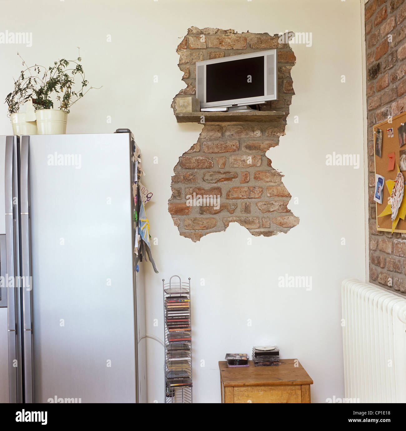 Contemporary brushed steel refrigerator and wall mounted T.V on cream wall with exposed