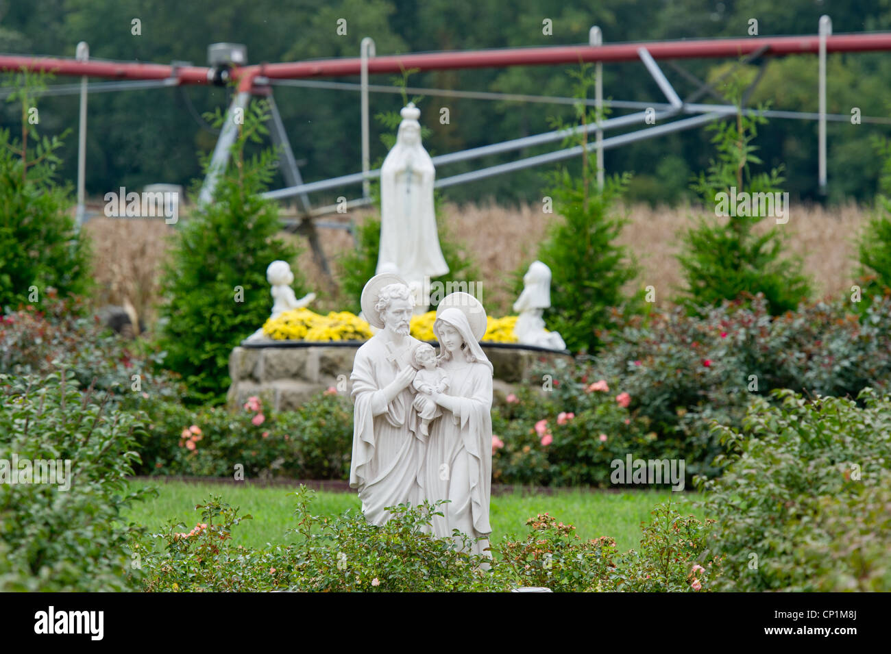 Irrigation system over corn crop behind Christian lawn ornaments on farm Stock Photo
