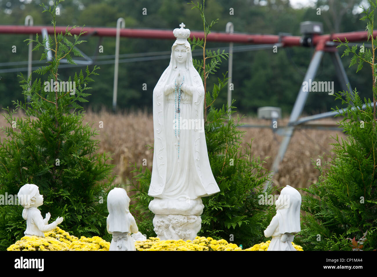 Irrigation system over corn crop behind Christian lawn ornaments on farm Stock Photo