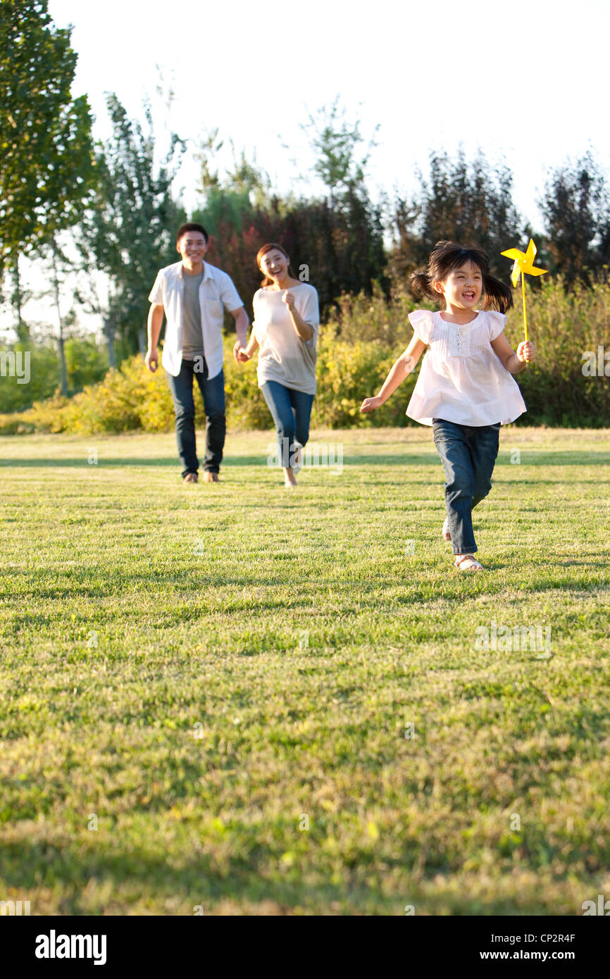 Young Chinese girl playing in a field with a pinwheel with her family ...