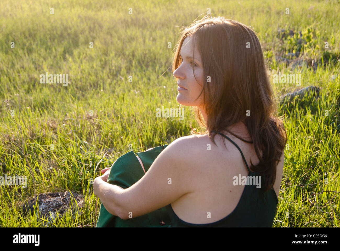 Young woman wearing green sits on the grass in the countryside Stock Photo