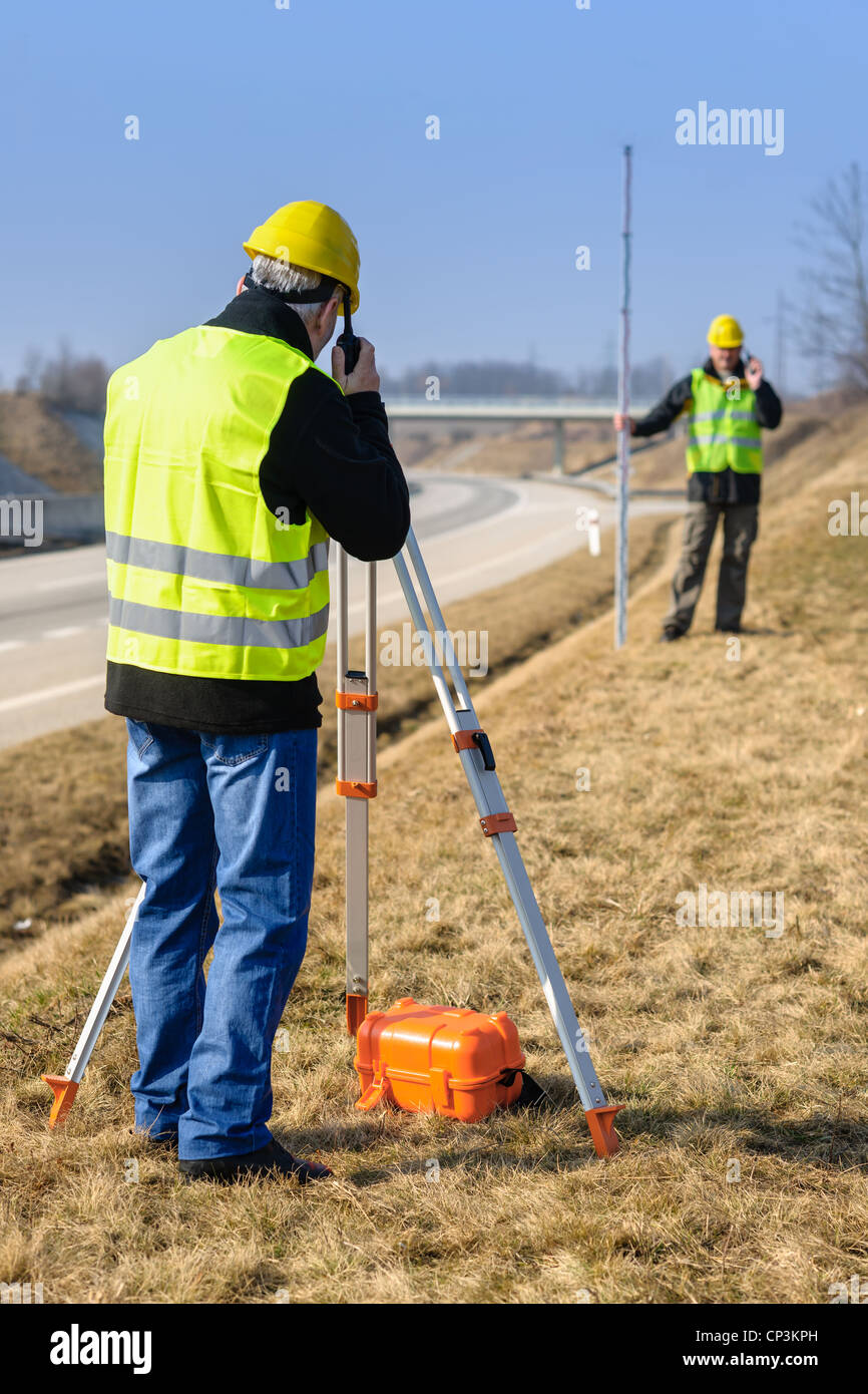 Land surveyors measuring with tacheometer speaking through transmitter